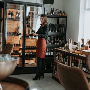 Eine Frau steht vor dem Weinkühlschrank und hält eine Weinflasche in der Hand.