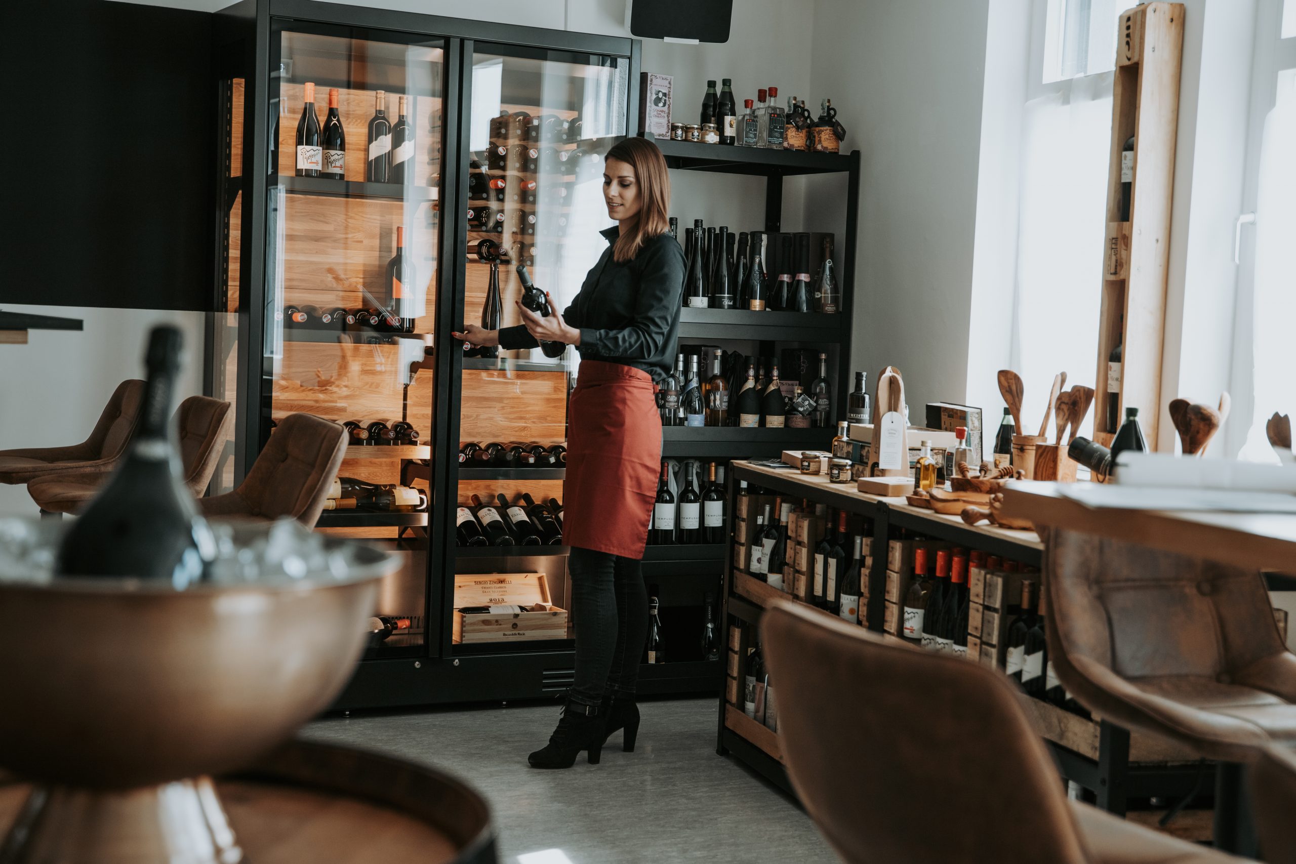 Eine Frau steht vor dem Weinkühlschrank und hält eine Weinflasche in der Hand.