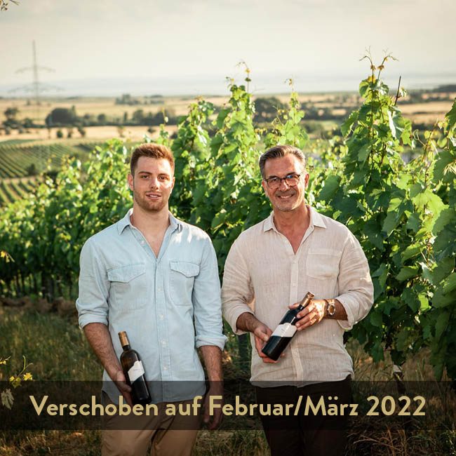 Vater und Sohn stehen im Weingarten und halten eine Flasche in der Hand.